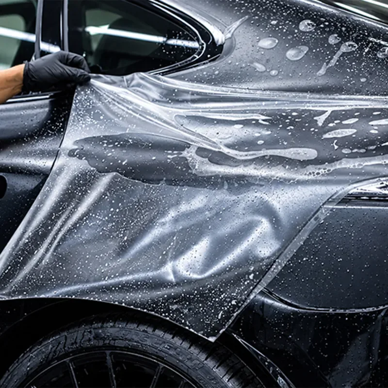 Detailer fitting clear paint protection film to a black car
